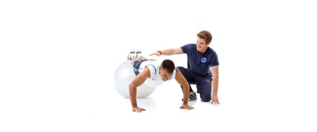 Fitness Trainer Assisting Client. Alt text: Personal trainer helping client perform a core exercise with a stability ball at Anthony Bevington Fitness in Brighton & Hove.