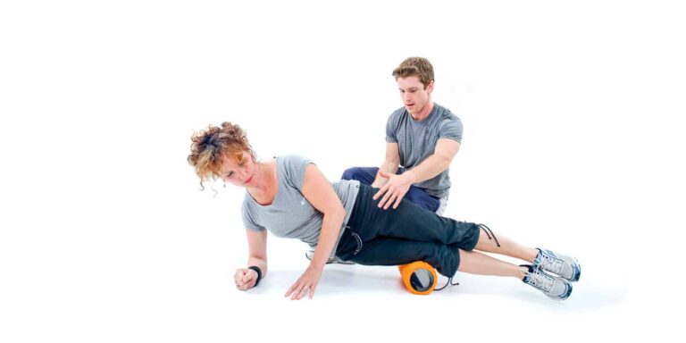 Personal trainer assisting woman with foam roller exercise for muscle recovery.